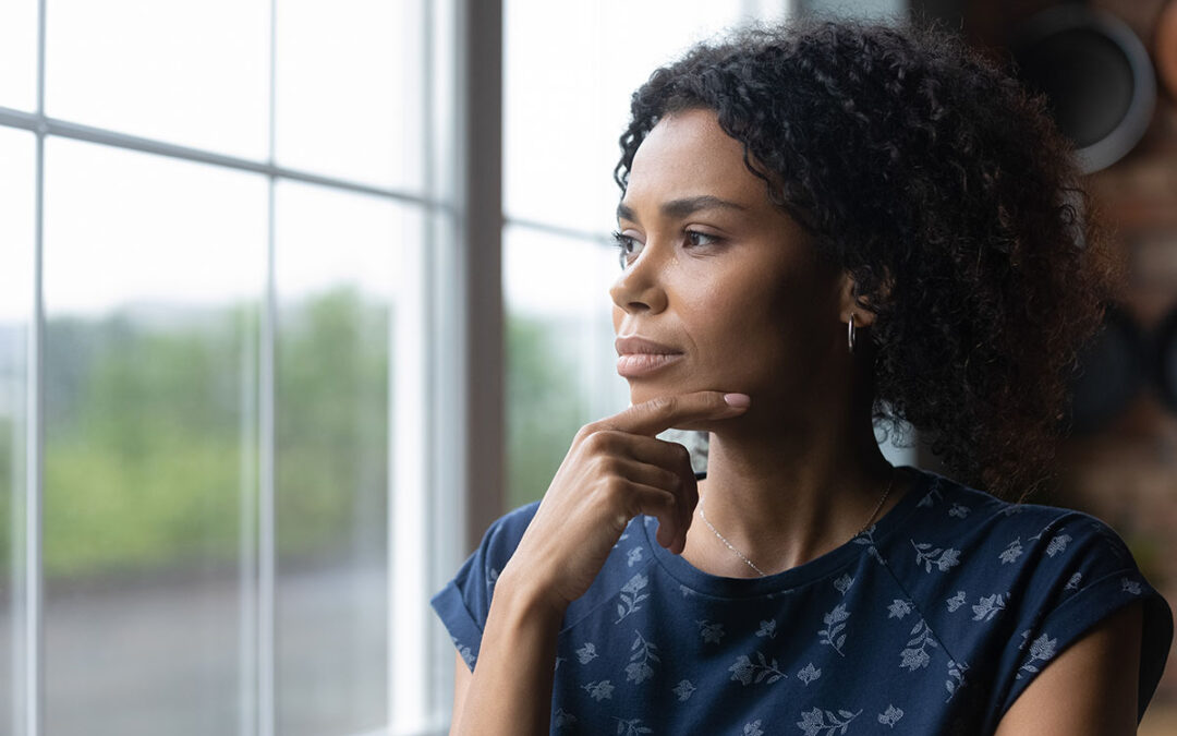 Thoughtful millennial african american woman standing near window, recollecting memories or feeling lonely at home